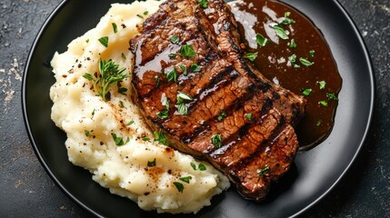 Plate of food consisting of a steak and mashed potatoes. the steak is cooked medium-rare and has a golden brown crust on the outside. it is garnished with chopped herbs and a drizzle of brown sauce.