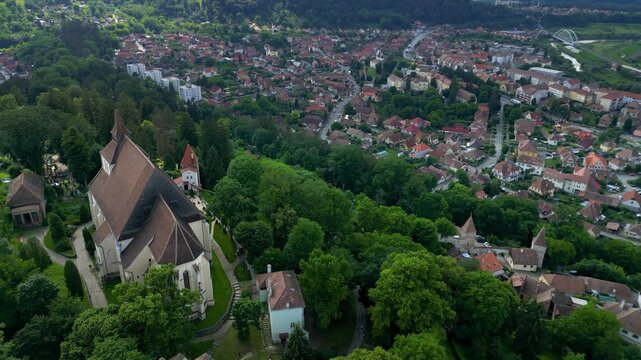 Aerial view of Sighisoara historic city center. Popular tourist destination and UNESCO World Heritage Site. Green landscape. City surrounded by forest. Drone going forward above the city center.