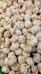 Garlic close up in supermarket. Lots of garlic in plastic green box on market stall. Garlic in green plastic box at farmers market. Garlic for sale in store. Display of fresh produce for sale