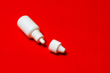 A white bottle, a vial for eye and nasal drops on a red background.