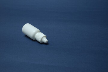 A white bottle, a vial for eye and nasal drops on a blue background.