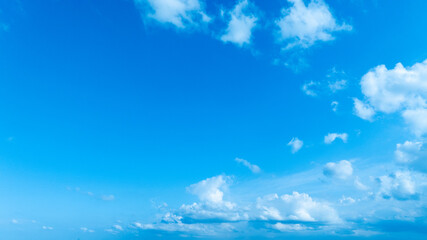 A bright blue sky with delicate white clouds floating, evoking a peaceful and refreshing summer feeling.