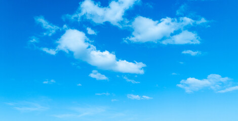 A warm and cheerful blue sky scattered with fluffy white clouds, symbolizing the beauty of a sunny...