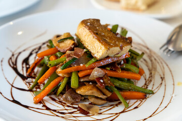 Assortment of cooked vegetables with duck liver on top and modena vinegar for decoration gourmet dish in Spanish restaurant