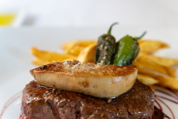 Grilled beef sirloin with duck liver on top green padron peppers and fries on plate Spain