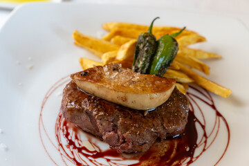 Grilled beef sirloin with duck liver on top green padron peppers and fries on plate Spain