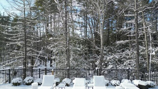 aerial view of snow covered lounge chairs next to closed shuttered swimming pool in winter (back yard patio loungers outdoor furniture) spa bizzard snowy snowfall frozen home countryside drone footage