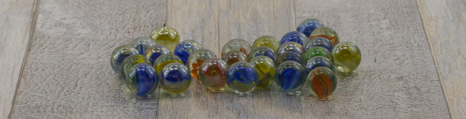 Panoramic view of a vibrant assortment of glass marbles, each uniquely patterned, artfully arranged on a rustic wooden surface that enhances their rich, colorful details