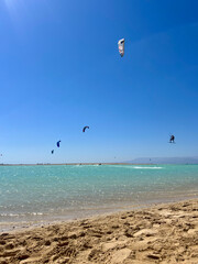 Man jumps high in the air while kitesurfing in Egypt with other kite-surfers in the background on a sunny day in summer with a clear blue sky. Wide shot