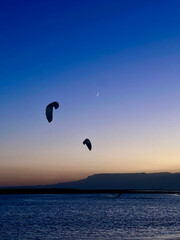 Silhouette of a kite surfer kiting on sunset with the moon view in the background in Egypt 