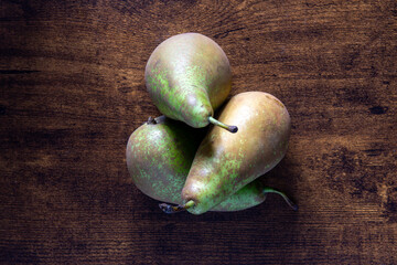 Three green pears are sitting on a wooden table. The pears are ripe and ready to eat