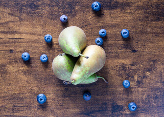 A bunch of pears and blueberries on a wooden table. The pears are green and the blueberries are blue