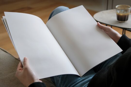 Person Holding an Open Blank Book While Sitting Indoors
