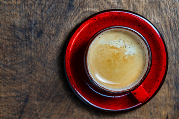 Tasty black coffee in red cup on wooden background, top view, closeup, copy space