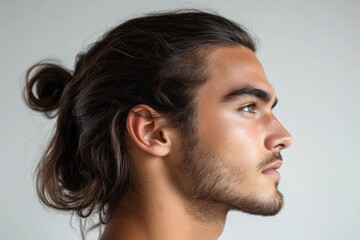 Fototapeta premium Close-up profile of a young man with long brown hair tied in a bun, highlighting his facial features and hairstyle against a simple background