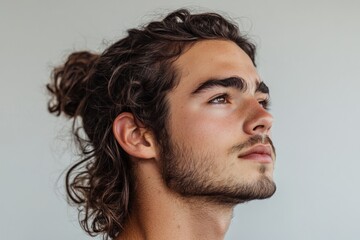 Close-up portrait of a thoughtful young man with long brown hair tied in a bun, gazing upwards