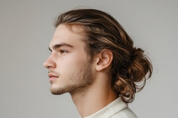 Fototapeta premium Profile of a young male model with long brown hair tied in a bun, showcasing a trendy hairstyle