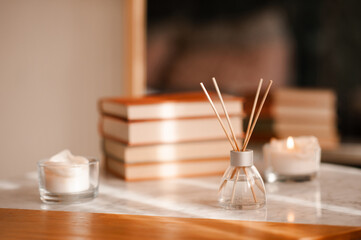Liquid home fragrance in glass bottle with bamboo sticks staying on marble coffee table over candle and stack of books in room close up. Aromatherapy.