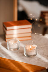 Scented burning candle with stack of paper books on marble table in room close up. Aromatherapy.