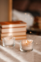 Scented burning candle with stack of paper books on marble table in room close up. Aromatherapy.