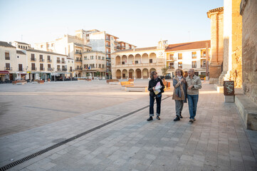 Obraz premium Three senior friends strolling through a sunny historic square, enjoying a relaxed sightseeing experience