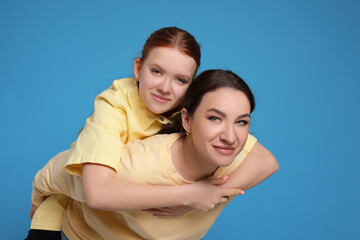 Fototapeta premium Portrait of beautiful mother with teenage daughter on light blue background