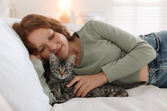 Beautiful teenage girl with cute cat on bed at home