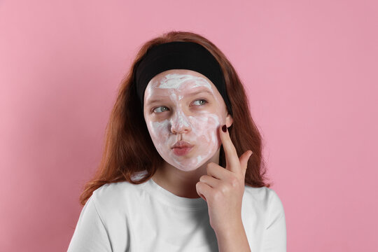 Teenage girl applying mask on her face with against pink background. Cosmetic product