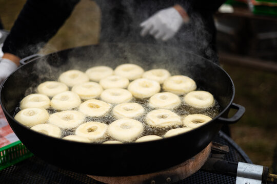 Delicious doughnuts frying in large pan at outdoor fair