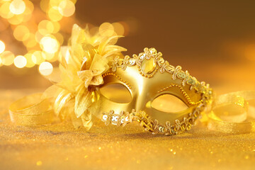 Naklejka premium Beautiful carnival mask on golden shiny surface against blurred lights, closeup