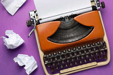 Vintage typewriter with sheet and crumpled paper on purple background, top view