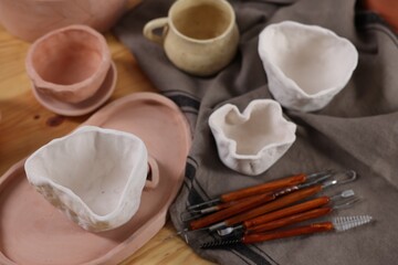 Set of different clay crafting tools and pottery on wooden table, above view