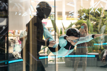 Excited teenage girl in helmet flying in aerodynamic tube wind tunnel. Skydiving training.