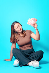 A cheerful woman sits on the floor holding money, showcasing feelings of happiness and success