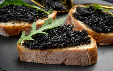 Pieces of crispy bread with luxurious black caviar and fresh arugula, served on a stylish black plate
