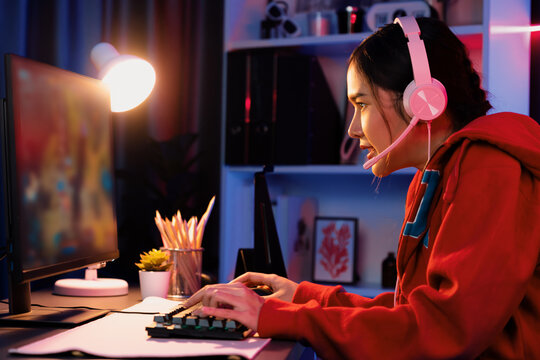 Host channel of young beautiful Asian gaming streamer playing fighting Moba at battle arena game on pc screen with multiplays, wearing pastel headphone at neon digital light modern room. Stratagem.