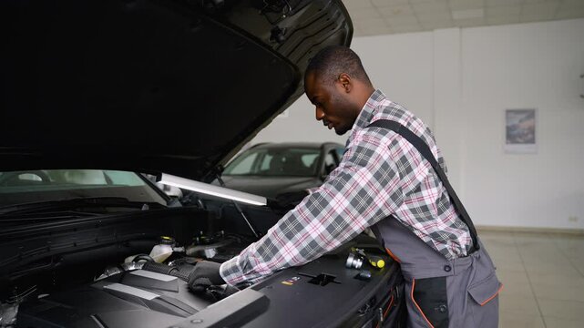 Auto mechanic inspecting car engine with work lamp