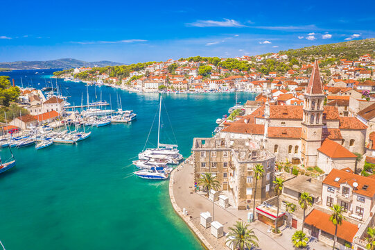 A drone view of Milna on Brač Island, Croatia, featuring the Church of Our Lady of Annunciation and its bell tower, a scenic bay filled with boats, a vibrant waterfront, and traditional Mediterranean 