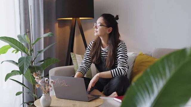 Driven young woman opens her laptop with a spark of inspiration, ready to dive into work. A perfect blend of ambition, creativity, and productivity in a modern setting