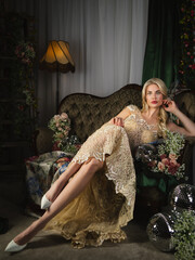 An elegant blonde in a luxurious embroidered evening dress poses in a vintage interior surrounded by flowers. A glamorous look, sophistication, aristocratic charm, and a romantic atmosphere.