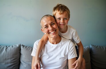 Young woman with bald head, son happily embracing on couch at home. Look directly at camera. Mother, child relaxed, smiling. Family support, positive emotions evident. Image moment of comfort, love.