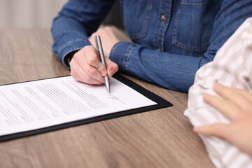 Woman putting signature on document at wooden table, closeup