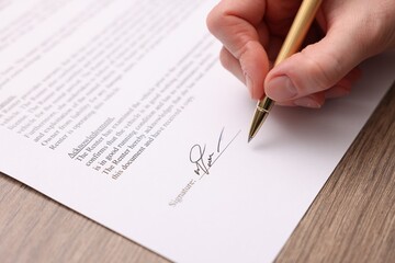 Woman putting signature on document at wooden table, closeup