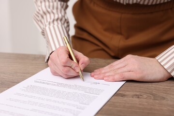 Woman putting signature on document at wooden table, closeup