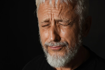 Sad senior man crying on black background, closeup. Space for text