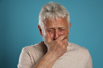 Sad senior man crying on light blue background