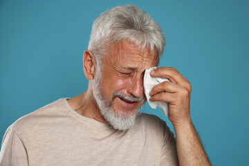 Sad senior man crying on light blue background