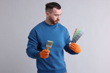 Man with paintbrush and color selection chart on light grey background