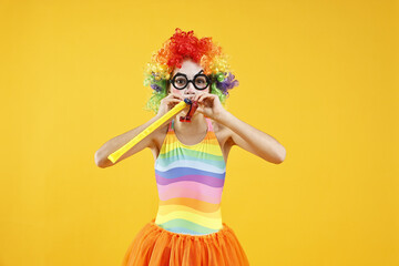 Girl dressed like clown with blowers on yellow background. Surprise party