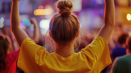 Crowd cheering and celebrating at a lively outdoor event, with focus on a young woman in yellow shirt raising her arms, enjoying the vibrant atmosphere.